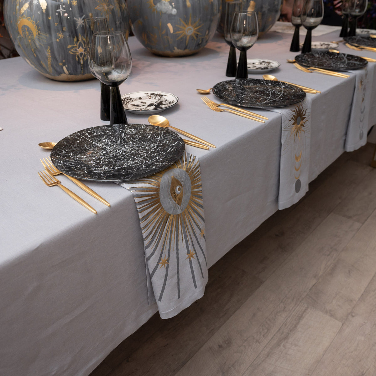 A table dressed in gray Zodiac linen with illustrated napkins and gold details
